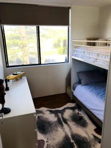 悉尼Manly family executive apartment的一间卧室配有一张双层床、一张桌子和一个窗户。