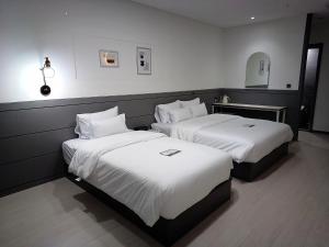 平泽市Hi& Hotel的配有白色床单的酒店客房内的两张床