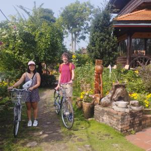 芹苴Brown House Resort的两名妇女站在花园里,骑着自行车