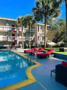 塔拉哈西Casa Bella Inn & Suites Extended Stay的一个带红色椅子和棕榈树的度假游泳池