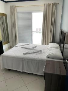瓜鲁雅Apartamentos Primavera Guarujá的一间卧室配有一张带白色床单的床和一扇窗户。