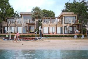 三百岭Marine Stay Pool Villa @300yod สามร้อยยอด的一对夫妇在房子前面的海滩上散步