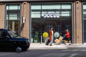 伦敦YOTEL London City的两个人在商店前带着行李沿着街道走