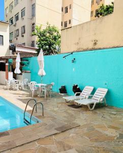 里约热内卢Hostel Estação Maracanã的蓝色墙壁旁的游泳池,配有椅子和遮阳伞