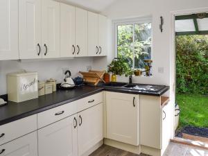 SoutergateWoodburn Cottage的厨房配有白色橱柜和黑色台面