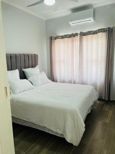 哈博罗内Zanaya Apartments的一间卧室配有一张带白色床单的床和一扇窗户。