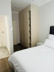 哈博罗内Zanaya Apartments的卧室配有一张白色大床和木制橱柜。