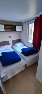 CamuracChalet et mobil homes dans la montagne au Camping les Sapins的一间卧室配有两张带蓝色枕头的床和窗户。