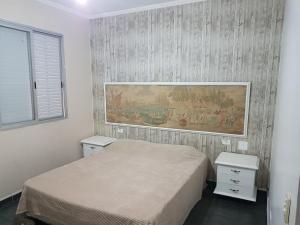 瓜鲁雅Apt. Enseada Guarujá的卧室配有一张床,墙上挂有绘画作品