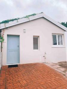 德班Stunning 1 bed cottage in Durban North的白色的房子,有蓝色的门和砖车道