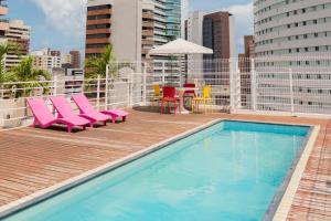 福塔莱萨D8 Hotel Express的一座游泳池,里面设有粉红色的椅子和一张桌子