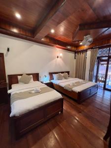 琅勃拉邦Chaluenxay Boutique hotel的客房内设有两张床,铺有木地板,拥有木制天花板。