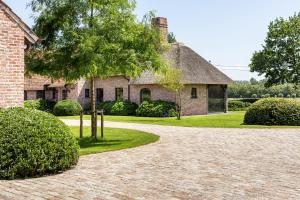 达默Hoeve den Akker - luxueuze vakantiewoningen met privétuinen en alpaca's nabij Brugge, Damme, Knokke, Sluis en Cadzand的砖屋,有树和车道