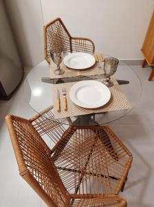 伊塔卡雷Flat Canto dos Pássaros的一张玻璃桌,上面有两把椅子和盘子