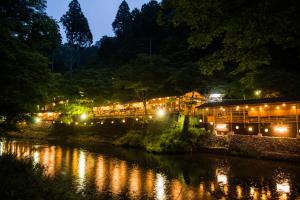 京都Momijiya Honkan Takaosansou的夜间在河边的一座有照明的建筑