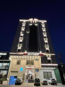 埃尔比勒Haden Hotel的一座高大的建筑,前面有汽车停放