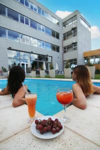 马拉圭Hotel Terra Patagonia的两个女人坐在游泳池边,喝着鸡尾酒和水果
