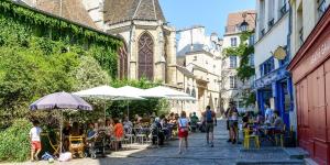 巴黎MARAIS CHIC heart of Paris, premium location !的一群人坐在街上的桌子上,与教堂同坐