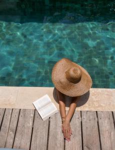 吉利阿尔La Siesta bungalows & Cuisine的一位戴帽子和书的女士,在游泳池旁边