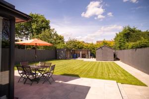 基德灵顿Orchid Lodge - Two Bed Generous Flat - Parking, Netflix, WIFI - Close to Blenheim Palace & Oxford - F4的庭院设有带雨伞的桌子和草坪。