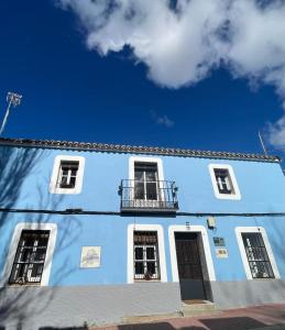 San RománCasa Rural Las Raíces, Sierra de San Vicente的蓝色的建筑,设有三扇窗户和阳台