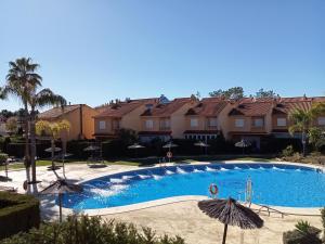 韦尔瓦Adosado playa Islantilla campo de golf的部分房屋前设有带遮阳伞的游泳池