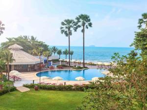 港生Novotel Rayong Rim Pae Resort的一座带遮阳伞的游泳池,其背景是大海