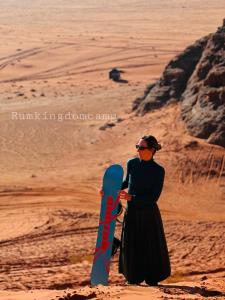 瓦迪拉姆Rum Kingdom Camp的站在沙漠中的妇女,拿着滑雪板