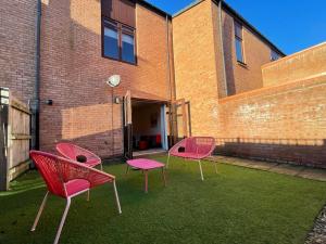 蒂斯河畔斯托克顿2 Bedroom House with Garden Next to River Tees的砖砌建筑前的草地上坐着三把粉红色的椅子