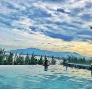 岘港Santori Hotel Da Nang Bay的一位女性在一座有山背景的游泳池里