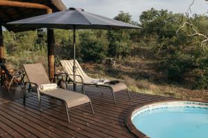 巴卢莱自然保护区Isambane Camp的游泳池旁的甲板配有两把椅子和一把遮阳伞