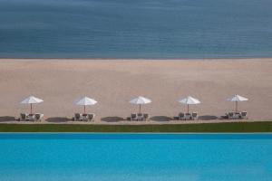 多哈The Chedi Katara Hotel & Resort的海滩上的一组椅子和遮阳伞