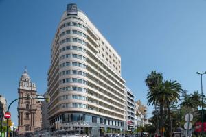 马拉加AC Hotel Málaga Palacio by Marriott的一座高大的白色建筑,位于一条种有棕榈树的城市街道上