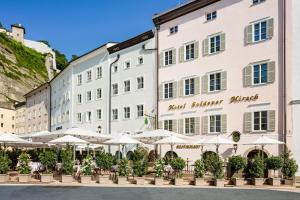 萨尔茨堡Hotel Goldener Hirsch, A Luxury Collection Hotel, Salzburg的一座带桌子和遮阳伞的大型白色建筑