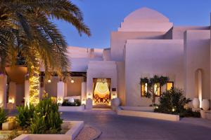 阿布扎比Al Wathba, a Luxury Collection Desert Resort & Spa, Abu Dhabi的一座白色的大建筑,前面有一棵棕榈树