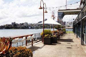 悉尼悉尼港1号码头傲途格精选酒店的一个带桌子和遮阳伞的临水露台
