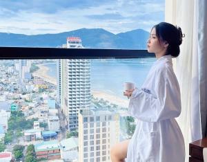 岘港Luxury Apartment in Sheraton Building with Ocean View的坐在窗户上拿着咖啡的女人