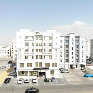 Al KhawḑSama Muscat Hotel的白色的建筑,有汽车停在停车场