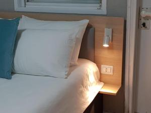 Or YehudaAirport Guest House的一张带白色枕头和灯开关的床