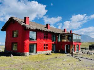 MachachiHotel Tambopaxi的田野上茅草屋顶的红色房子