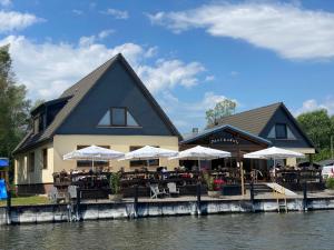 DargunAusflugsrestaurant & Pension Aalbude & Hausfloßvermietung am Kummerower See的河边餐厅,设有桌子和遮阳伞