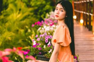 乌隆他尼Nakara Villas & Glamping Udon Thani的站在木人行道上,穿着橙色衣服的女人,花朵