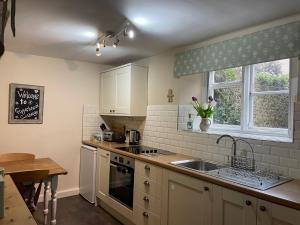 ChideockGingerbread Cottage的厨房配有白色橱柜、水槽和窗户。