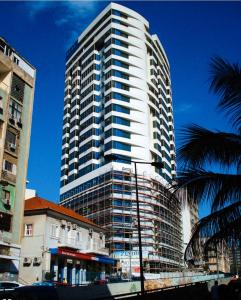 罗安达Apartamento com Vista para a Baía de Luanda的一座高大的白色建筑,前面有一棵棕榈树