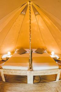 科尼尔-德拉弗龙特拉TAIGA Conil的一张大床,位于带两张桌子的帐篷内