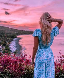艾湄湾Waenis Sunset View Hotel and Restaurant, Amed, Bali的穿着蓝色衣服的女人,看着大海