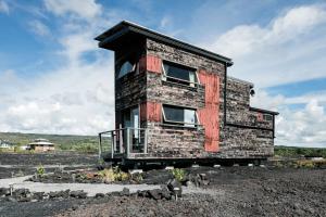 KehenaTHE PHOENIX HOUSE - EPIC Tiny Home Gem on Volcanic Lava Field!的砖屋,在田野上设有阳台