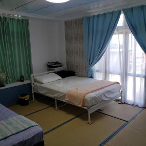 Arazato宮古島ゲストハウス　マウイ的一间卧室配有床和蓝色窗帘的窗户