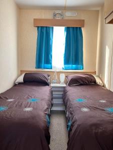 赫彻姆Lyntons 3 bedroom caravan pets stay free的配有蓝色窗帘和窗户的客房内的两张床