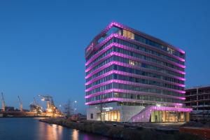 阿姆斯特丹Moxy Amsterdam Houthavens的一条河旁一座高大的建筑,上面有紫色的灯光